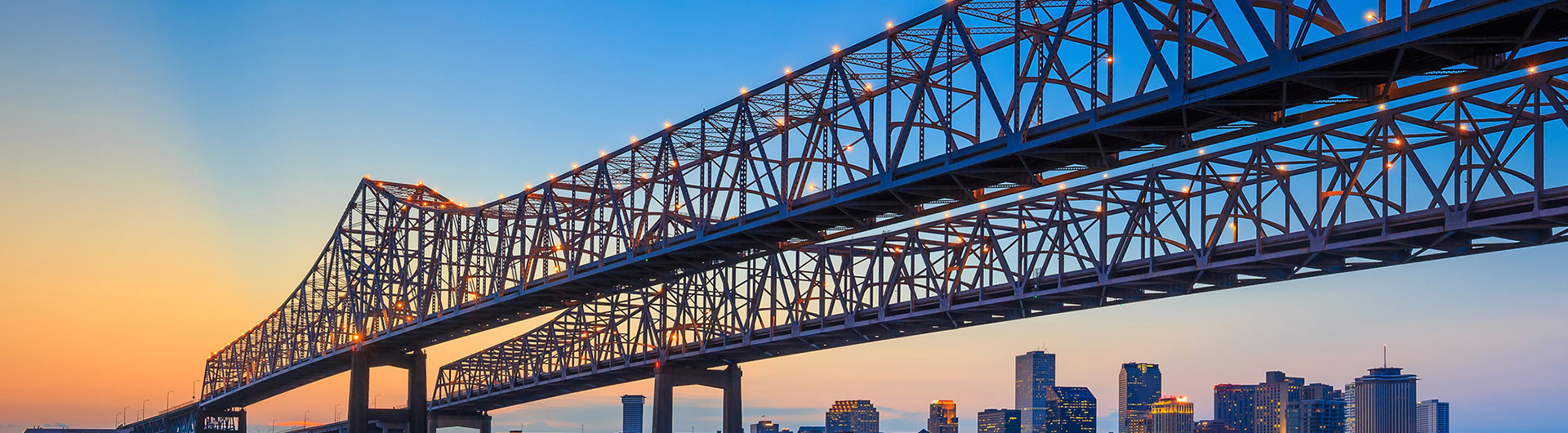 Twin cantilever bridge over the river at sunset with a city skyline beyond