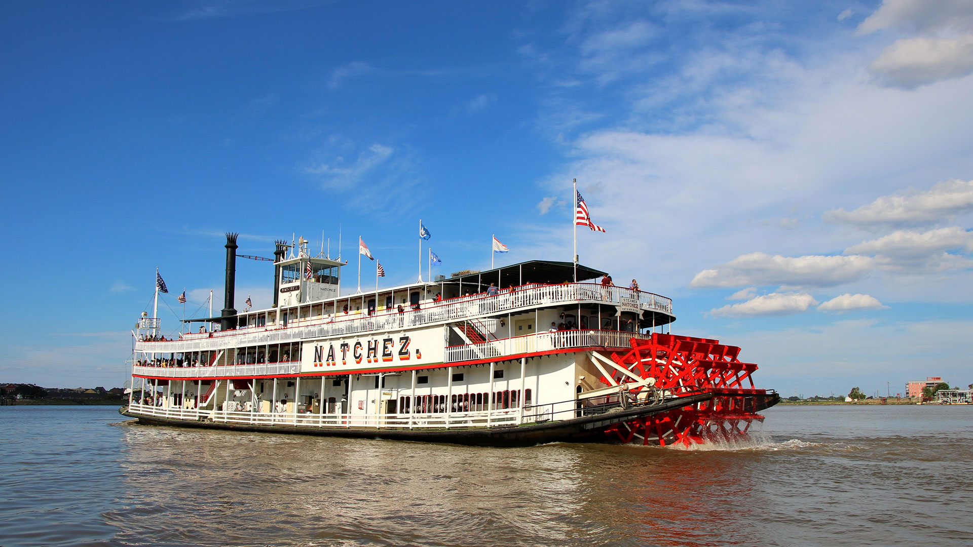 The steamboat Natchez churning along the river under a blue sky