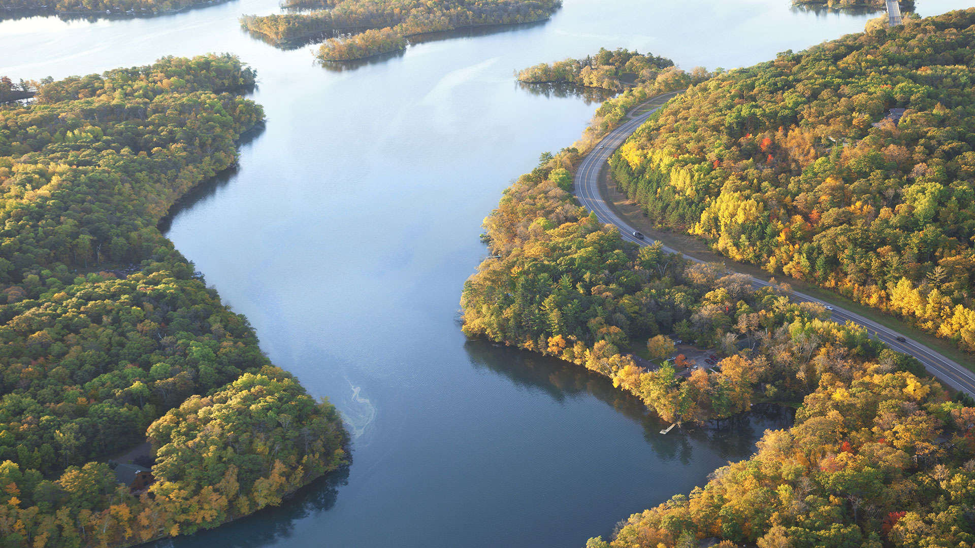Aerial view of a river winding between wooded bluffs in autumn colour